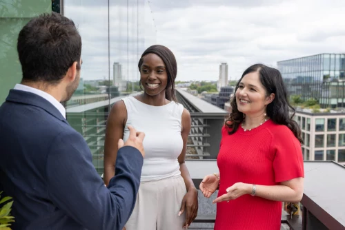 London law firm associates and partners networking outdoors on a rooftop terrace, smiling and engaged in conversation.